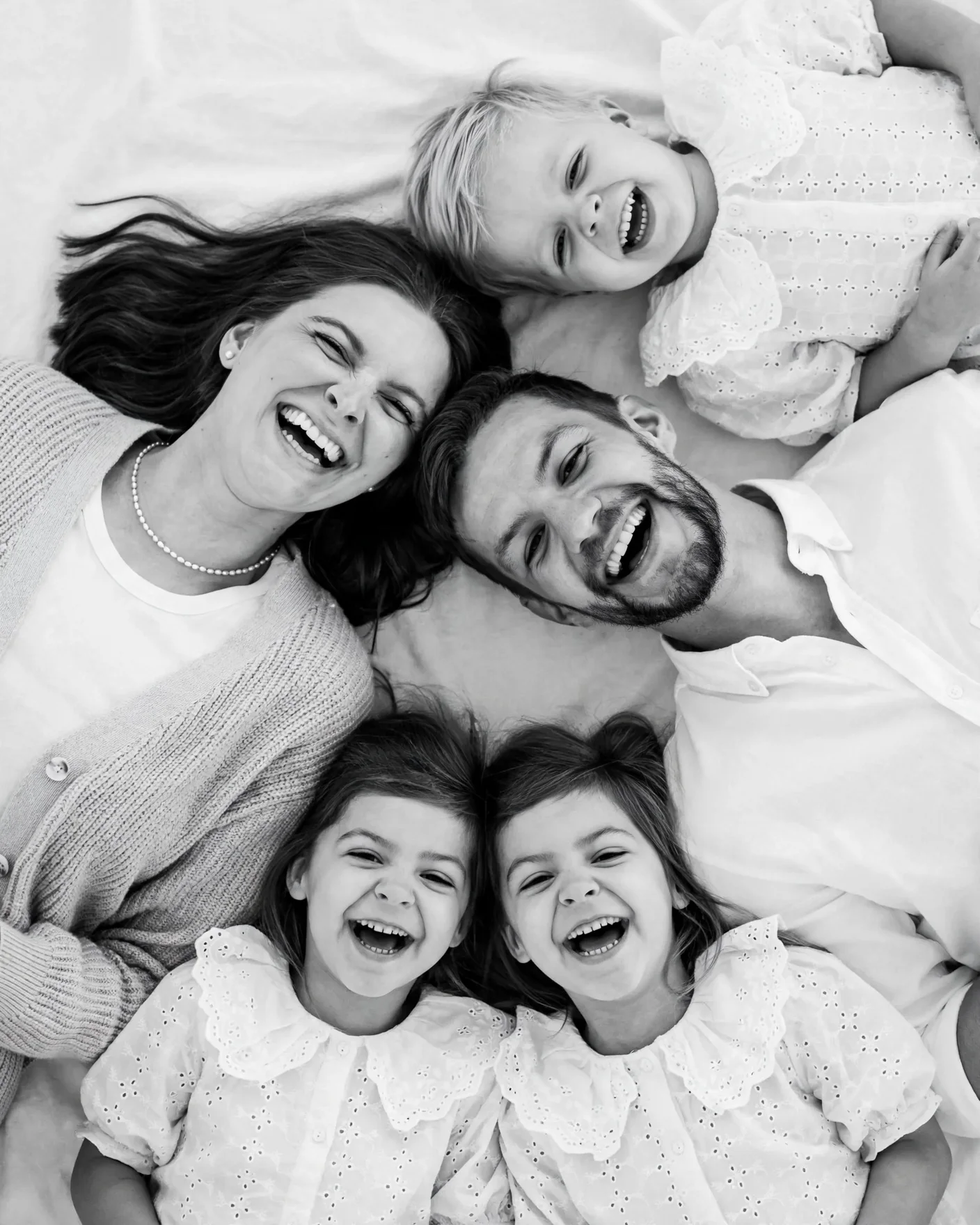 Черно-белое семейное фото сверху с улыбающимися родителями и детьми на светлом пледе