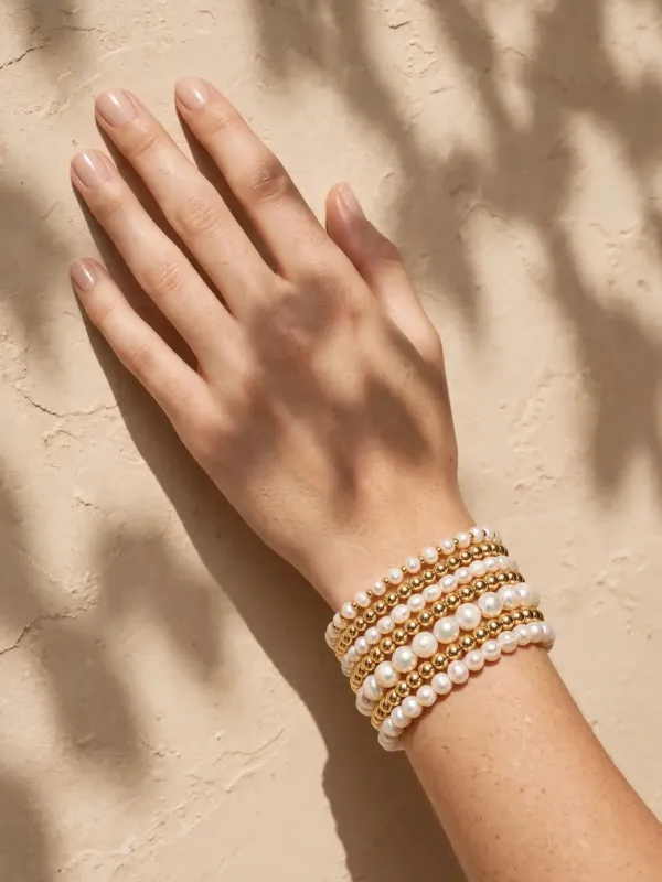 Фото браслетов из жемчуга и золота на руке модели при тёплом солнечном свете